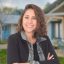 A woman smiling outdoors in front of modern houses, representing friendly community and home living.